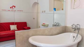 A modern bathroom with a freestanding bathtub, a red sofa with a cushion, and a mirror reflecting the room.