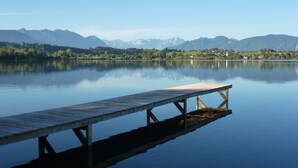 Un muelle de madera que se adentra en aguas tranquilas, con montañas y un cielo despejado al fondo.