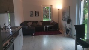 Un espacio habitable pequeño con kitchenette, un sofá, una mesa de vidrio y una silla.
