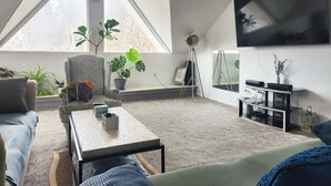 Un salon moderne avec une grande fenêtre, un canapé, une table basse et un téléviseur fixé au mur.