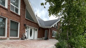 Une maison à deux étages, construite en briques, dotée de grandes fenêtres, d’un porche à l’avant et d’un jardin bien entretenu, agrémenté de paillis et de rochers.