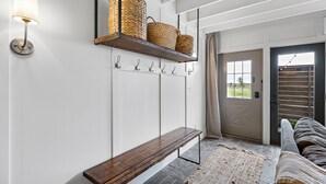 Ein Flur mit einer Bank, einem an der Wand befestigten Regal mit Körben, einer Wandleuchte und einer Tür mit Ausblick.