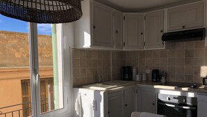 Una cocina compacta con armarios blancos, horno empotrado y cafetera.