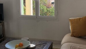 Una sala de estar con un ventanal grande, un sofá, una mesa de centro con frutas y un televisor.
