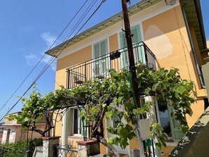 A yellow building with a balcony, a vine-covered wall, and visible power lines. - Terrace with stunning sea view and pergola with vines (Menton)