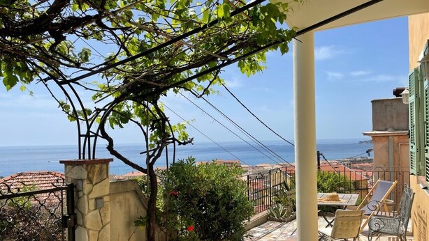 Una terraza con vista al mar, suelo de piedra, plantas en macetas y mobiliario de exterior.
