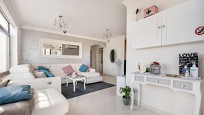 Ein modernes Wohnzimmer mit einer weißen Sofagarnitur, einem Couchtisch, einer Topfpflanze und einem weißen Konsolentisch mit Dekorationselementen.