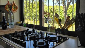 Una cocina con estufa a gas, una ventana con vista a árboles y utensilios de cocina sobre la encimera.