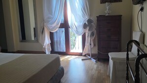 Un dormitorio con una cama, un aparador, una silla, un ventilador, un televisor y un cuadro en la pared.