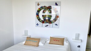 Un lit bien fait, avec du linge de lit blanc, deux oreillers ornés d’inscriptions, une œuvre d’art murale et une petite table de chevet avec une lampe.