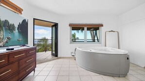 Ett rymligt rum med ett stort fönster som ger utsikt över båtar på vattnet, ett bubbelbad och ett träskåp med lådor.