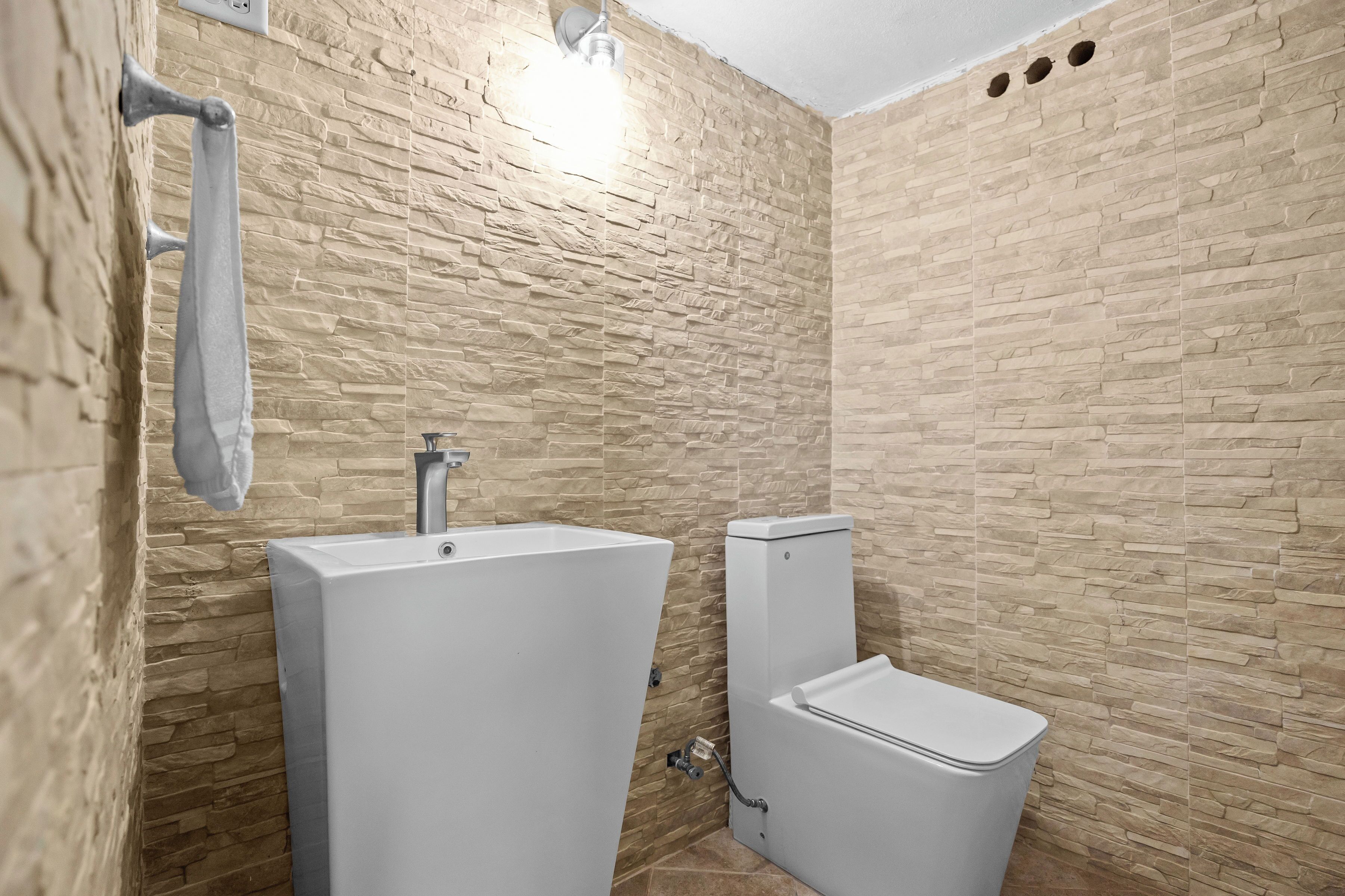 Een badkamer met een wand met steenstructuur, een witte wastafel en een toilet.