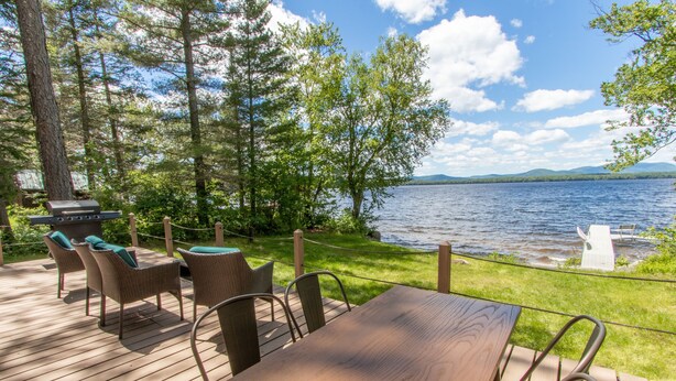 En terrasse med grill, fletstol og bord med udsigt over en sø.