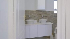 Moderni kylpyhuone, jossa on kaksi pesuallasta, peili ja laatoitettu seinäallas.