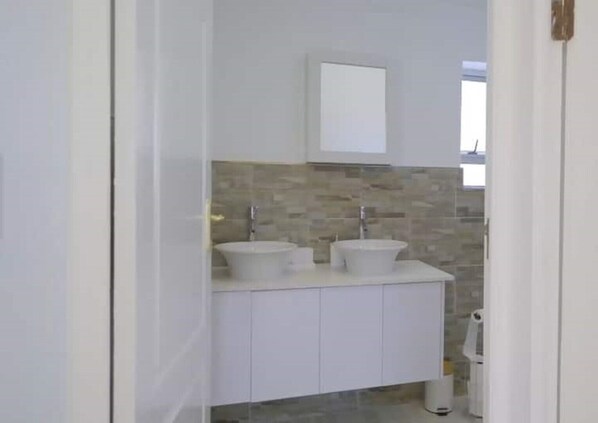 A modern bathroom with two sinks, a mirror, and a tiled backsplash.