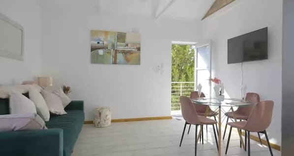 Una sala de estar moderna con un sofá verde, un comedor con sillas rosas y un gran ventanal.