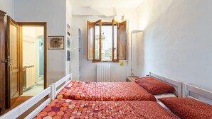 Une chambre avec deux lits, une fenêtre, un radiateur et une porte donnant sur une salle de bain.