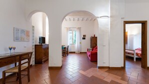 Un vaste espace de vie doté d’un parquet en point de Hongrie, d’un bureau en bois avec une chaise, d’un canapé rouge et d’un téléviseur.