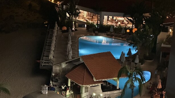 Zwembad van een resort met een prieel, palmbomen en een restaurant op de achtergrond.