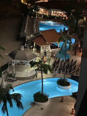 A resort pool area with a gazebo, palm trees, and a restaurant in the background. - LUXE OCEANSIDE VACATION CONDO  (Puerto Vallarta)