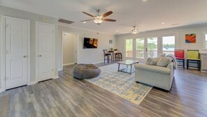A spacious living room with hardwood flooring, a grey sofa, a bean bag, a glass coffee table, and a ceiling fan.
