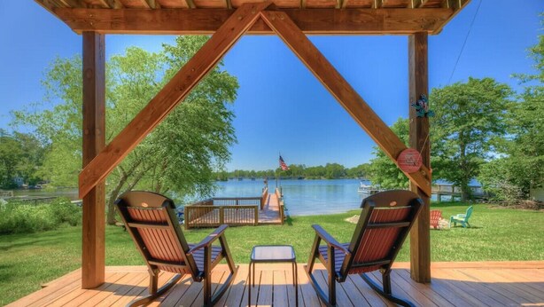 A wooden deck with two rocking chairs facing a lake, a dock, and a flag.