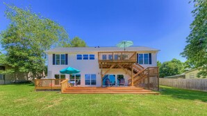 A two-story house with a wooden deck, a covered patio, and a staircase leading to the upper level.