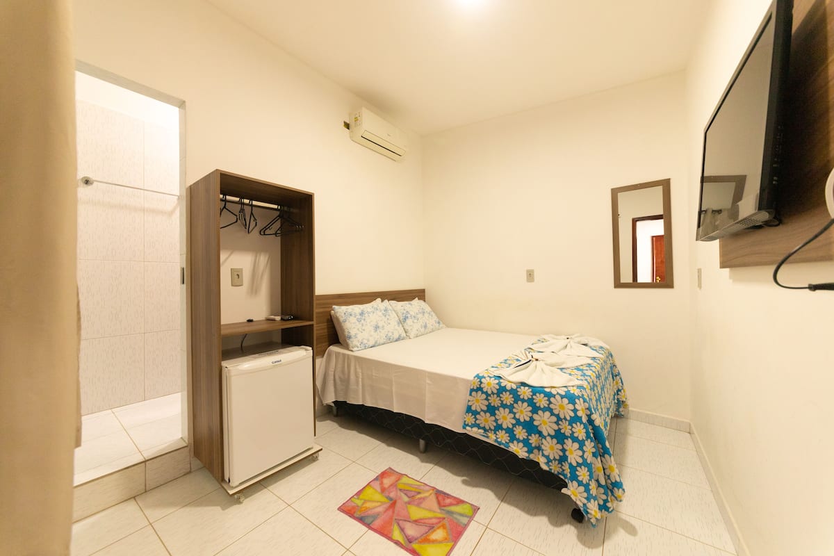 A small bedroom with a bed, a wardrobe, a small fridge, and a shower area.