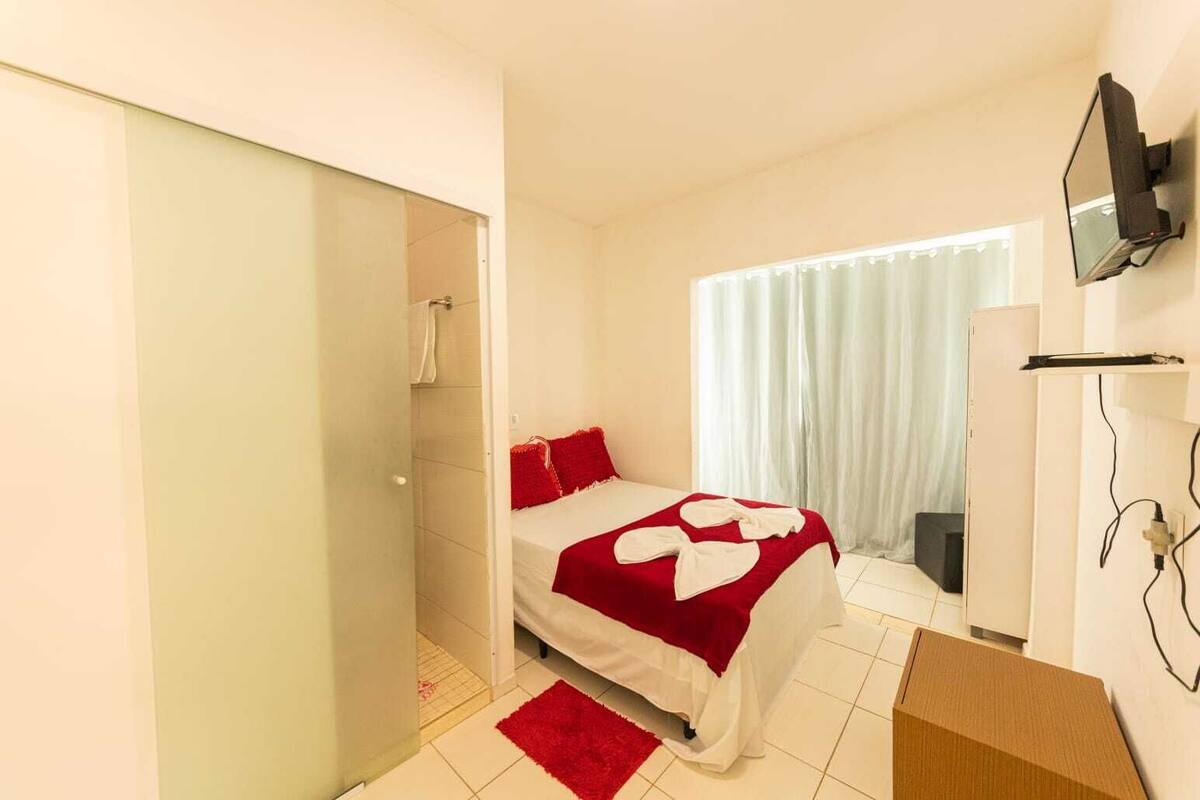A bedroom with a bed, a TV mounted on the wall, and a window with curtains.