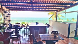 Un área de comedor al aire libre con mesas y sillas, con vista a la playa.