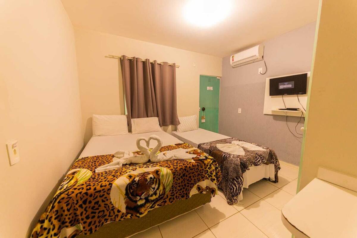 A hotel room with two beds, a TV, and an air conditioning unit.