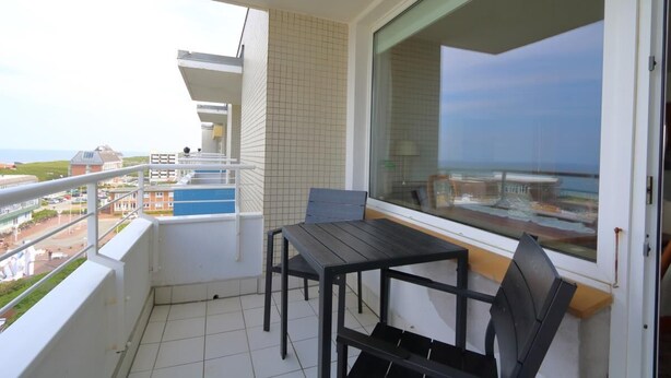 Un balcone con tavolo e sedie, vista sul mare e un muro piastrellato.