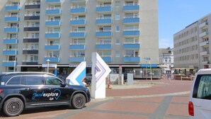 Un hotel a più piani con balconi, un'area di parcheggio e un cartello con frecce direzionali.
