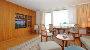 Un soggiorno con un mobiletto in legno, una televisione, un tavolo da pranzo con sedie e una finestra con tende.