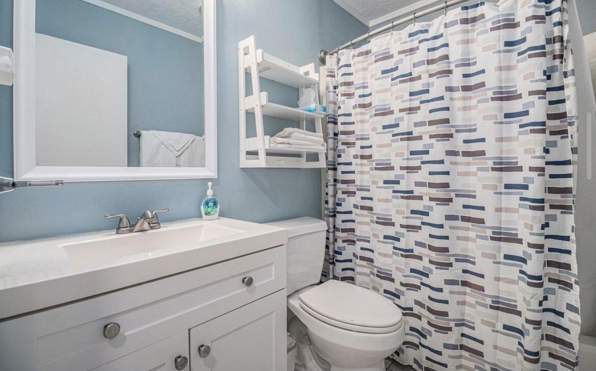 Une salle de bain avec un lavabo blanc, un miroir, des toilettes et un rideau de douche à motifs géométriques.