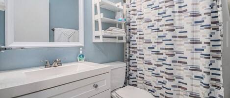 Une salle de bain avec un lavabo blanc, un miroir, des toilettes et un rideau de douche à motifs géométriques.