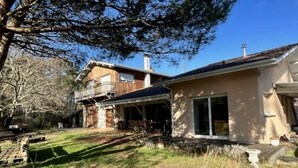 Een tweelaags huis met een overdekte veranda, een losstaande garage en een grote boom op de achtergrond.