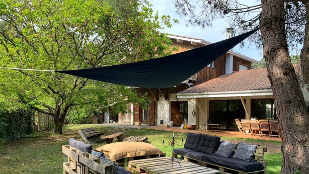 Een achtertuin met een houten terras, tuinmeubilair en een grote boom.