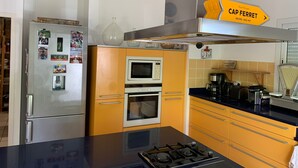 Een moderne keuken met een gasfornuis, dubbele ovens, een koelkast en een geel kastje.