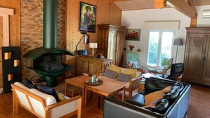 Een gezellige woonkamer met houten wanden, een open haard, een bank, een eettafel en een keukenhoek.