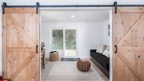 A room with a sliding barn door, a sofa, a patterned rug, and a wooden bench. - Hike & Bike Stowe | 7 Min to Town | AC | Hot Tub (Stowe)