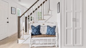 A staircase with a white bench at the bottom, white doors on either side, and a wooden handrail. - Hike & Bike Stowe | 7 Min to Town | AC | Hot Tub (Stowe)