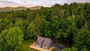 A single-story house with a deck, surrounded by dense forest. - Hike & Bike Stowe | 7 Min to Town | AC | Hot Tub (Stowe)