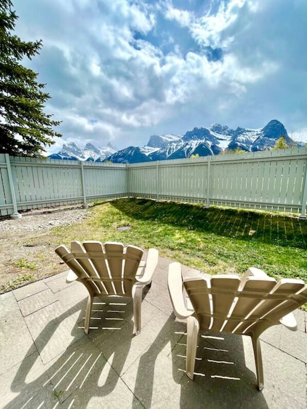 Un patio con sillas Adirondack orientadas hacia una vista de la montaña, rodeado por una cerca blanca.