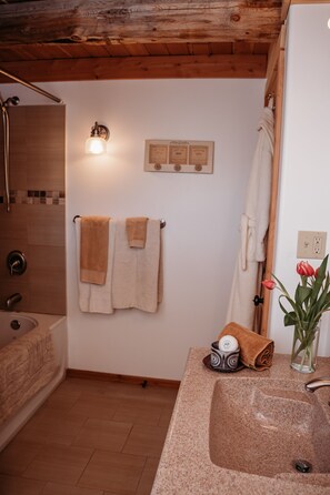 A bathroom with a wooden ceiling, a sink with a granite countertop, a towel rack with towels, a framed certificate on the wall, and a vase with a red tulip. - RockyMountainView BnB (Entrance)