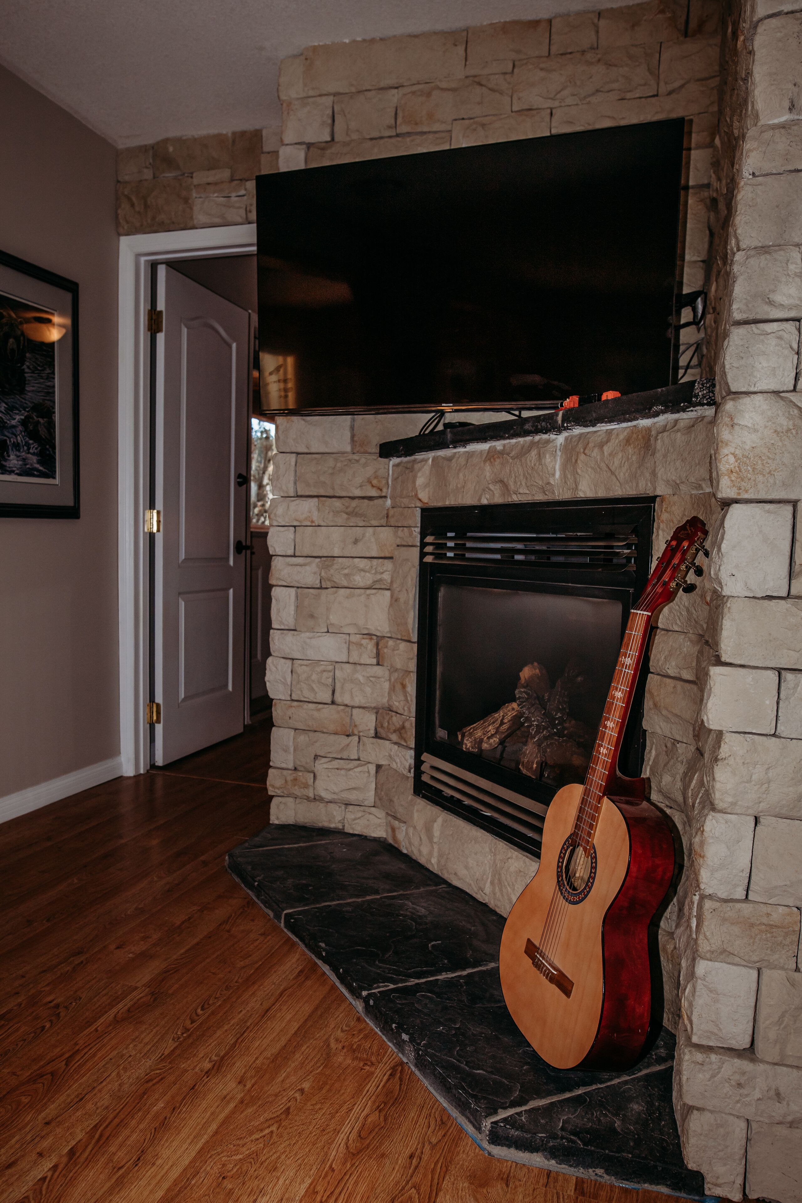 Una sala de estar con chimenea de piedra, televisor montado y una guitarra apoyada en la pared.