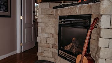 Una sala de estar con chimenea de piedra, televisor montado y una guitarra apoyada en la pared.