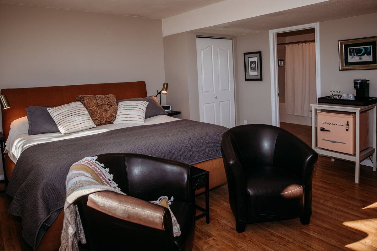 A bedroom with a bed, two chairs, a desk, and a wardrobe.