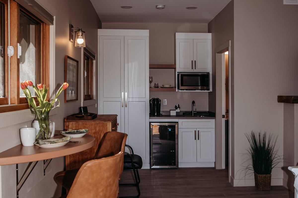 A modern kitchen with white cabinets, a built-in microwave, and a dining area with a wooden table and leather chairs.
