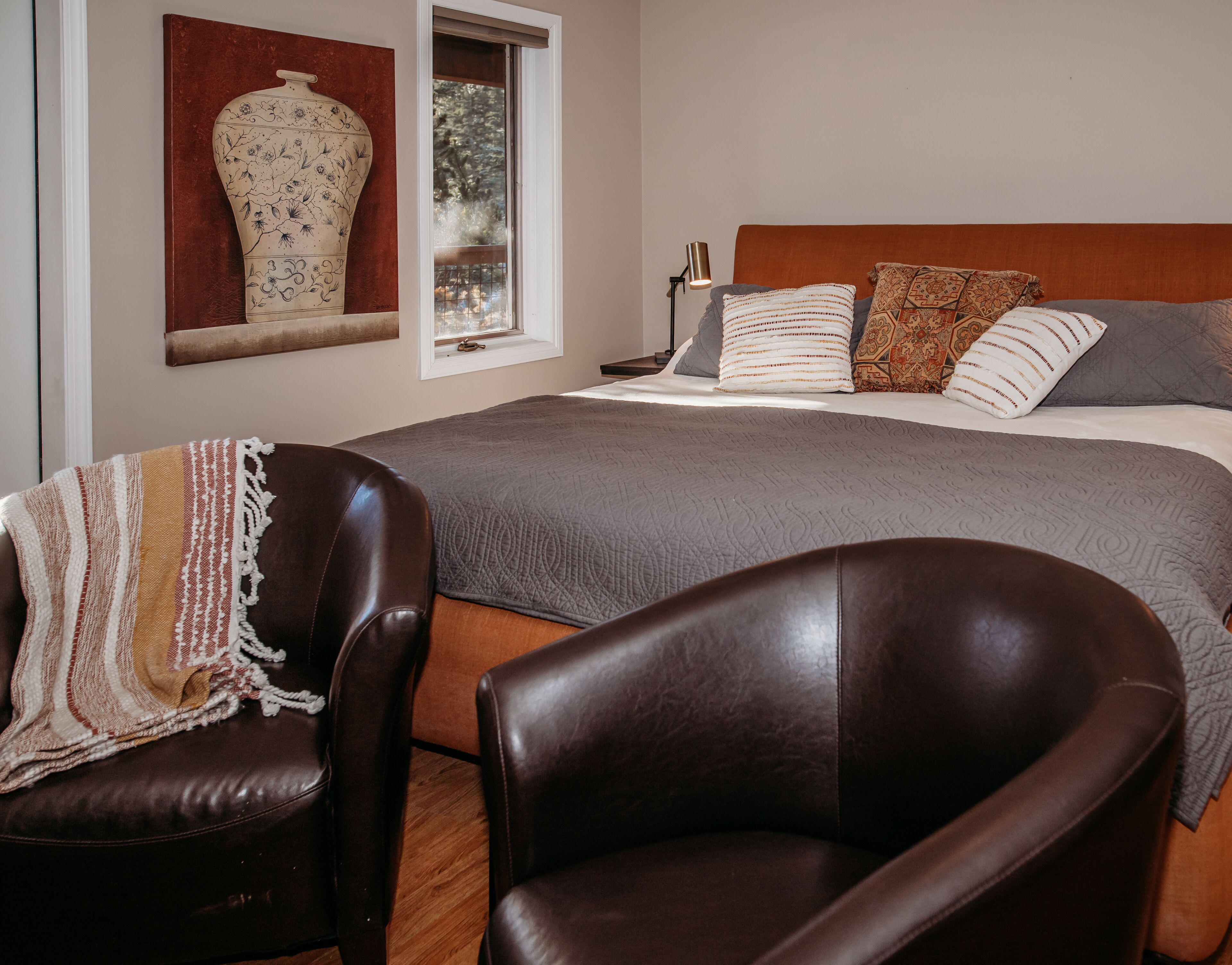 A bedroom with a large bed, a chair, a lamp, and a vase on the wall.
